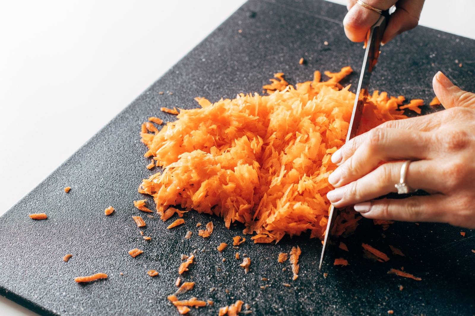 Chopping grated carrots on a cutting board.