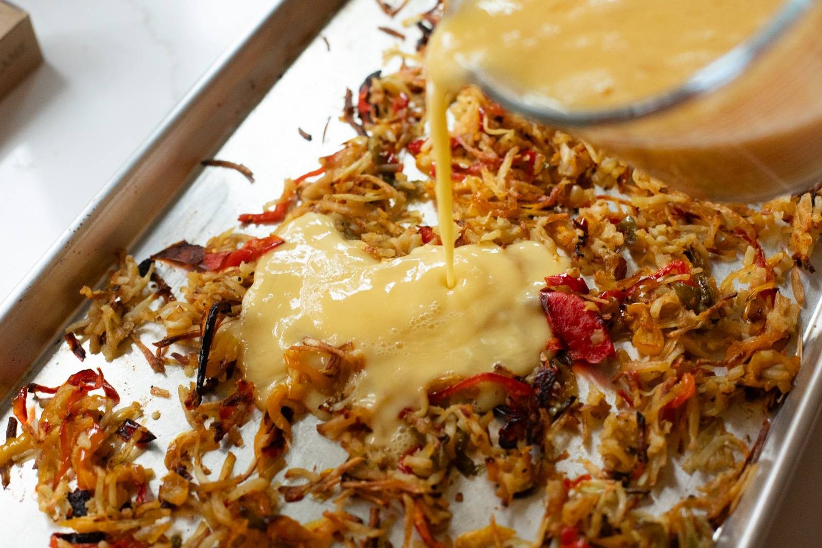 Pouring eggs onto the sheet pan with veggies.