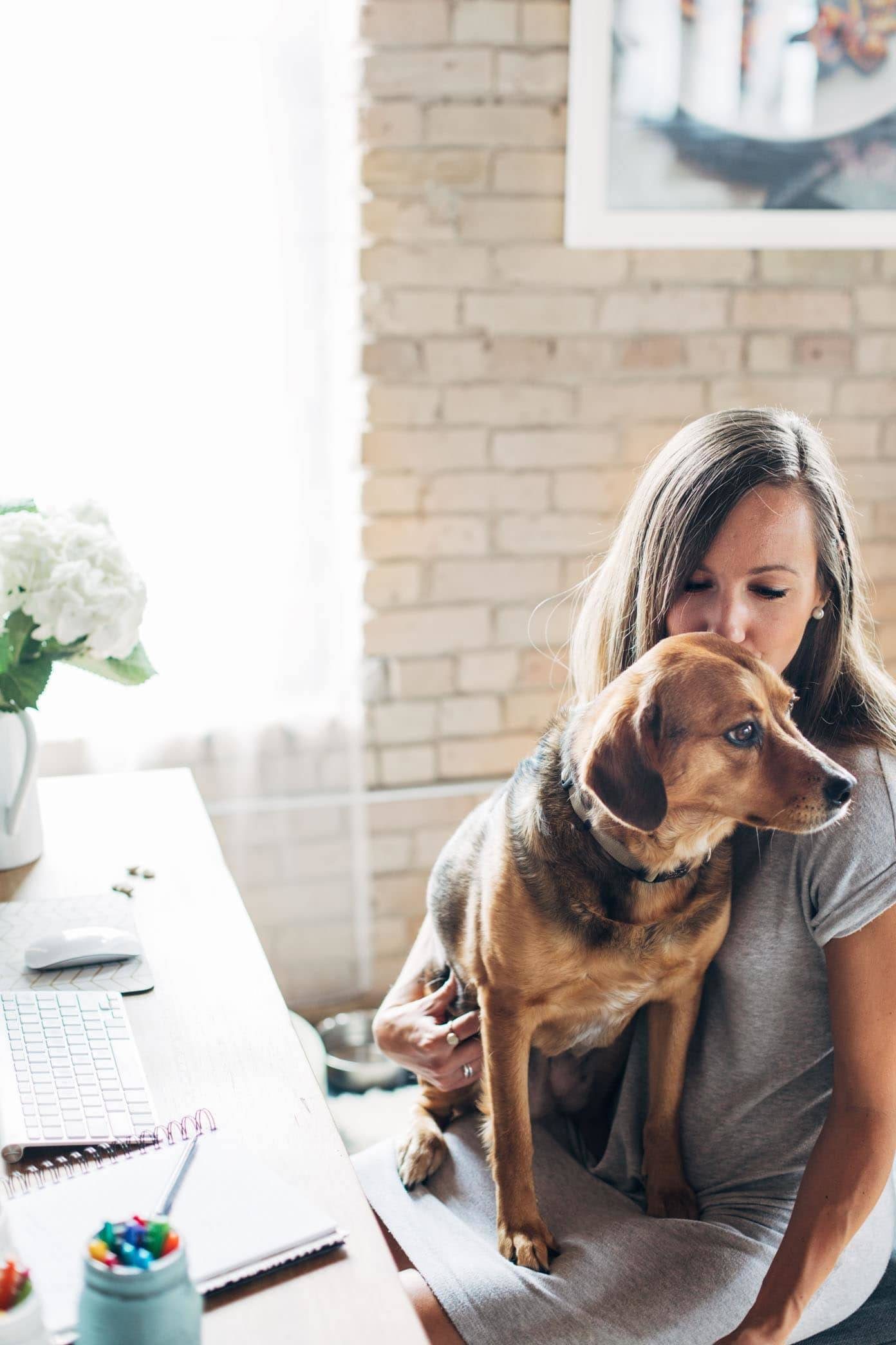 Woman sitting on a desk with a dog in her lap.