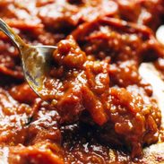 A spoon reaches into a tomato sauce.